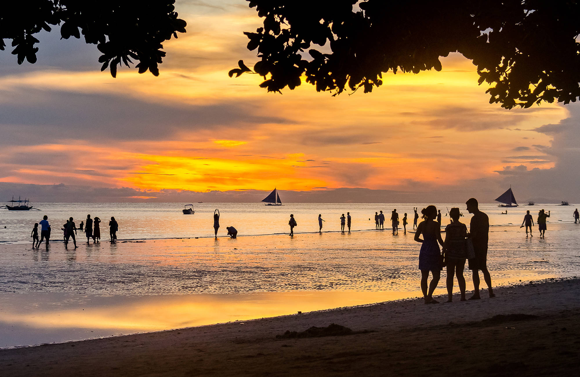 MÄnniskor vandrar i soldnedgången på en strand i Boracay.