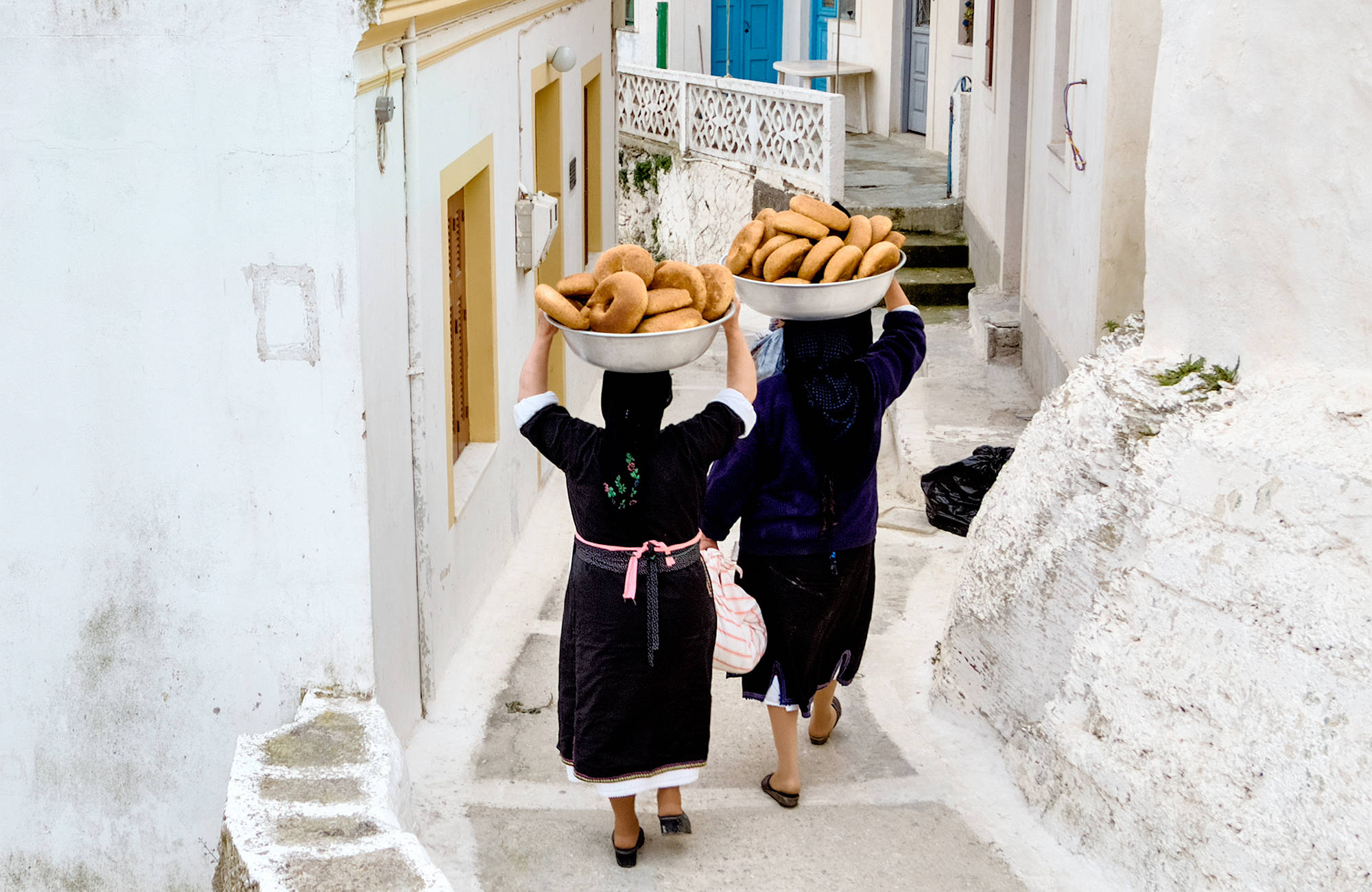 Två kvinnor bär på korgar med bröd i Grekland.
