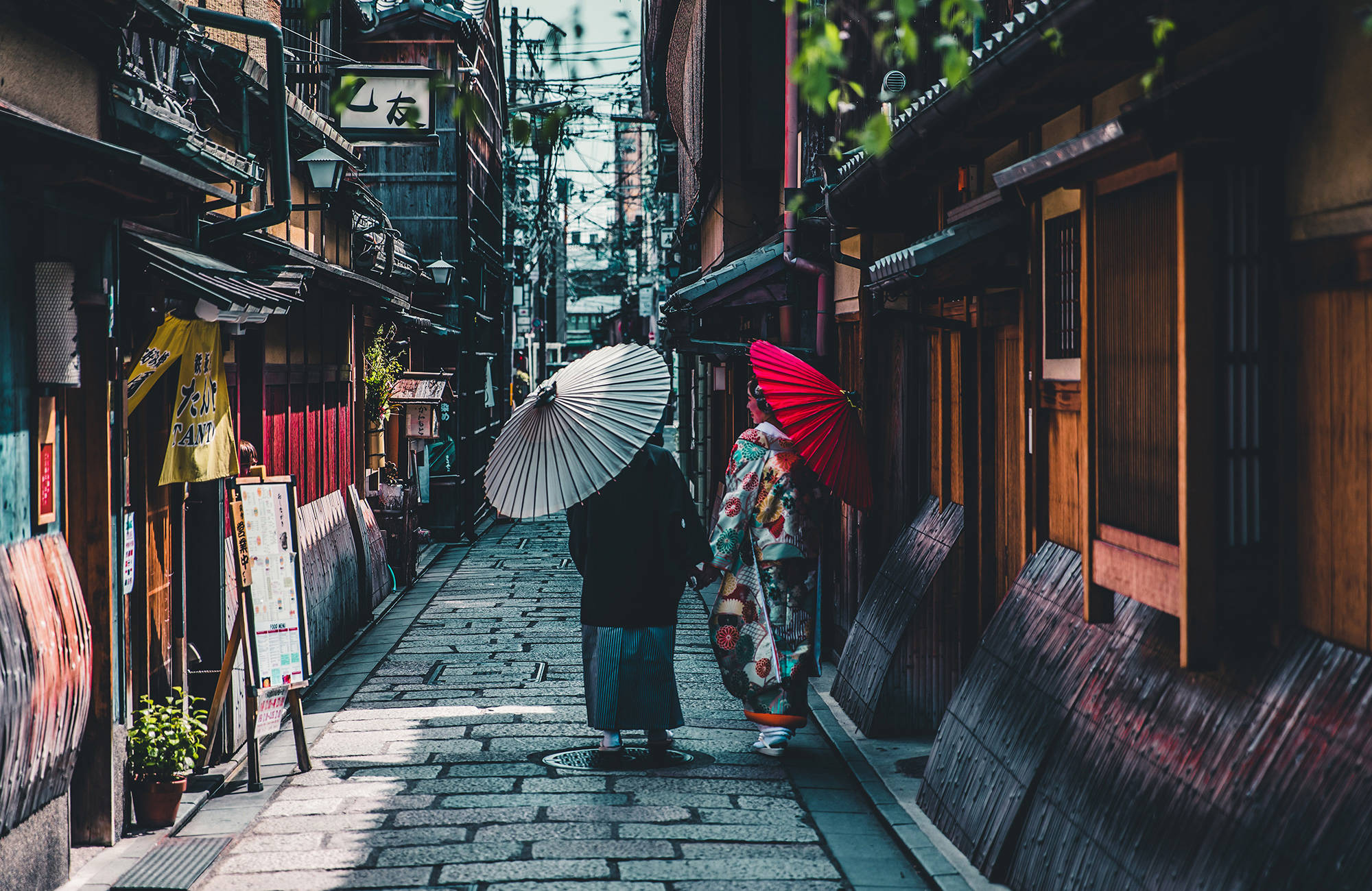 Två kvinnor promenerar på en kullerstensgata i Japan i traditionella kläder.
