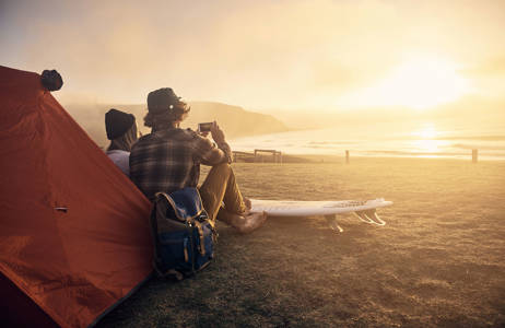 Kvinna och man med surfbrädor tältar på en strand i solnedgången i november.