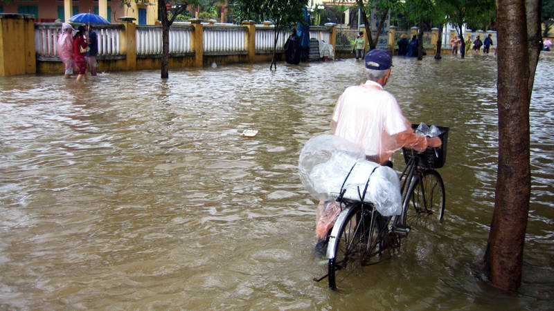 Man walking with a bike through a monsoon-flooded street in Asia.
