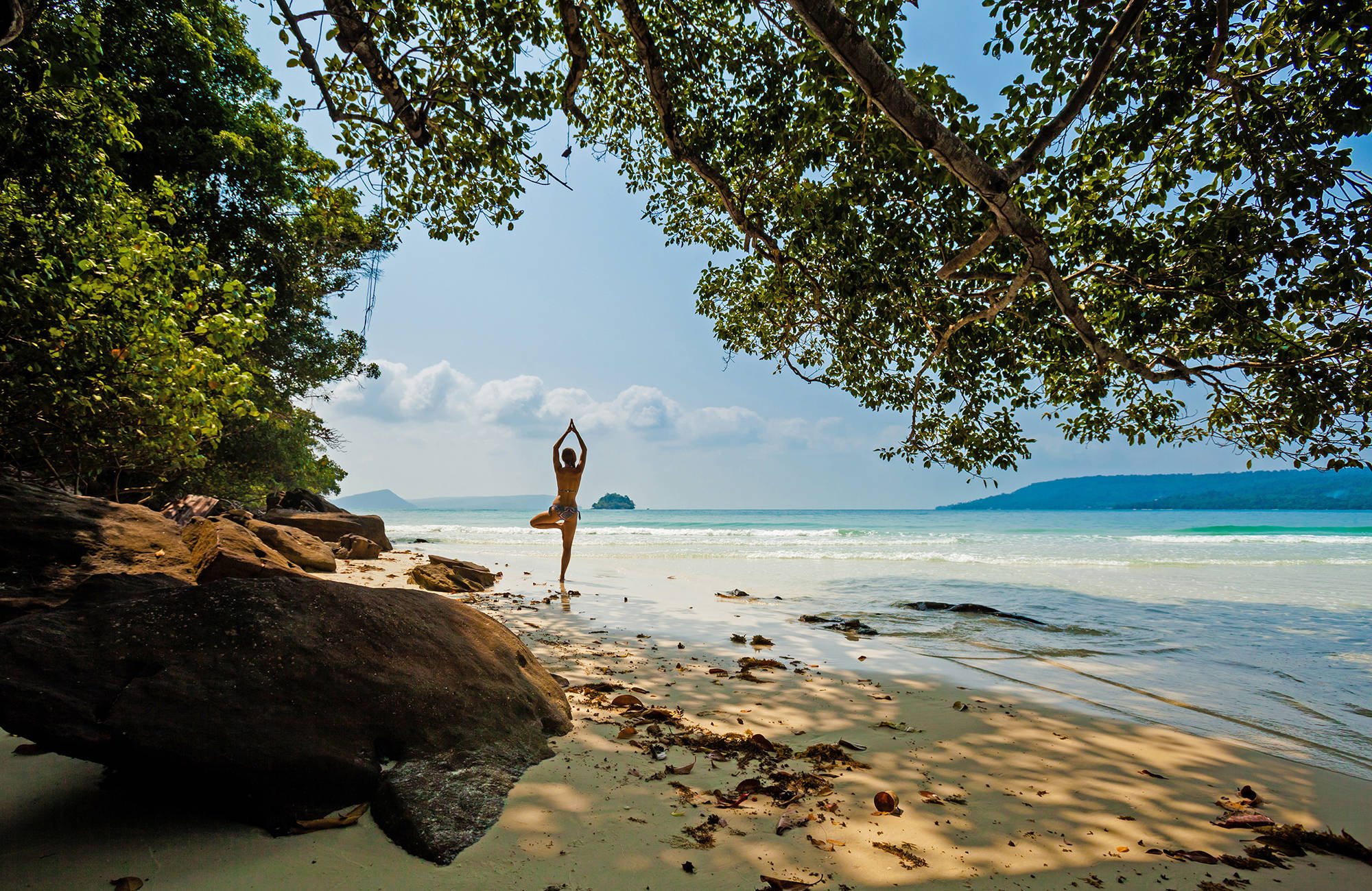 Vacker strand med träd och en person som utövar yoga.