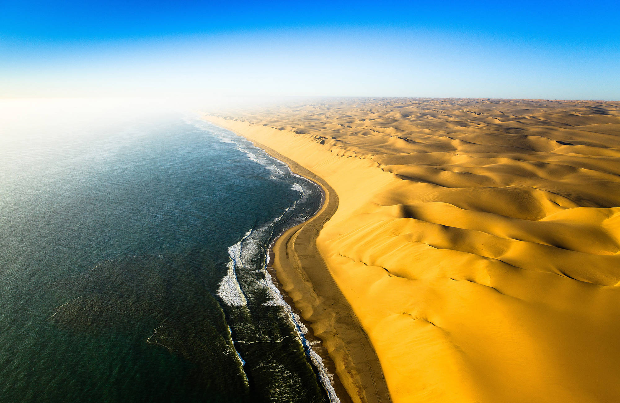 Vy från helikopter över havet som möter öknen i Namibia.