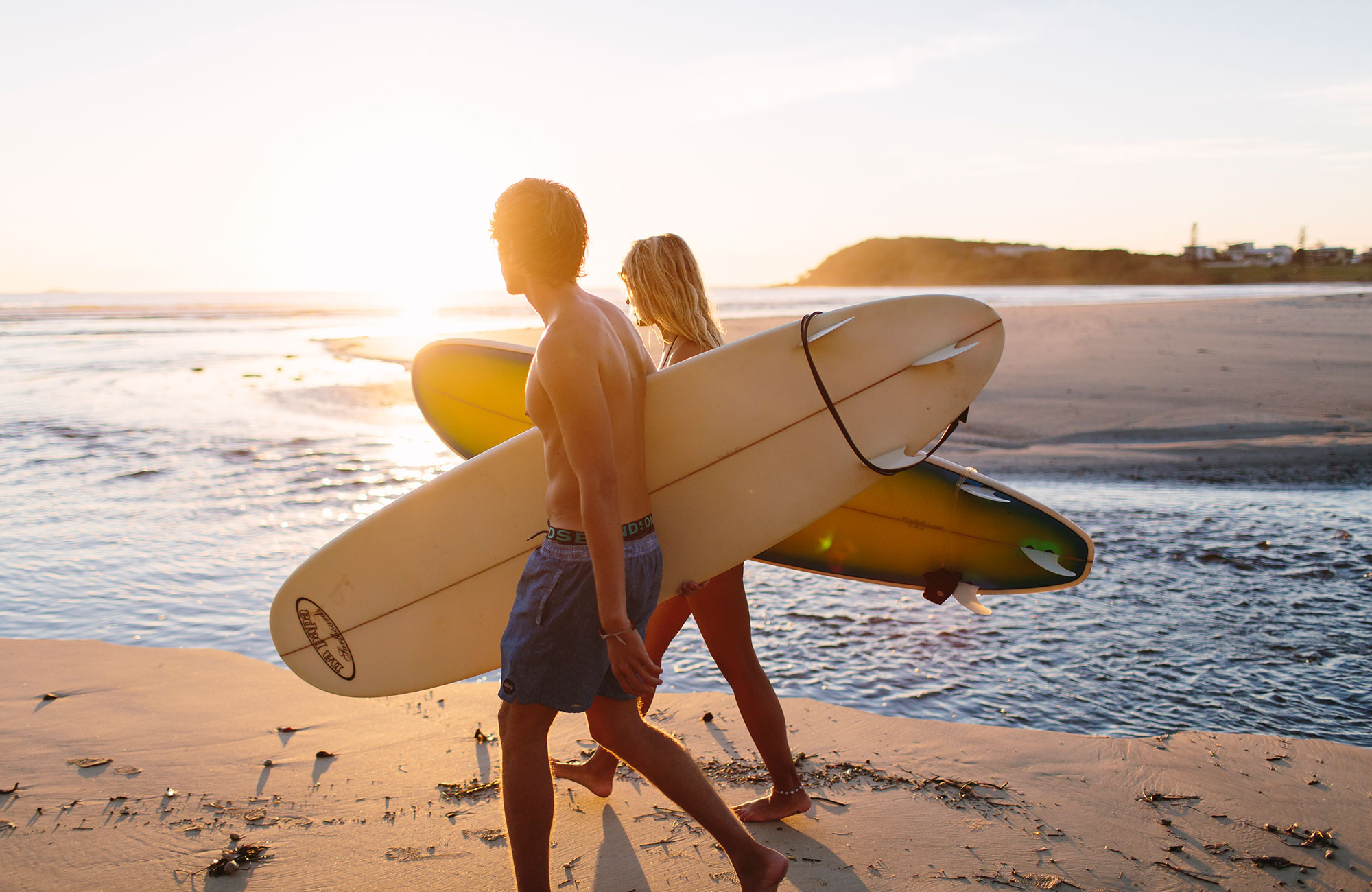 en man och kvinna i motljus som bär på surfbrädor