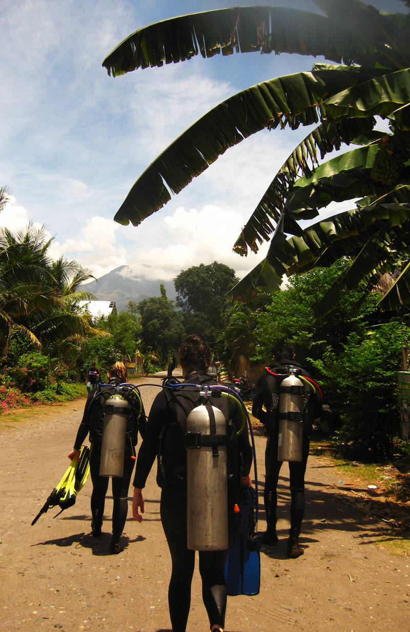 Divers walking with air tanks on their backs back from the ocean to the camp location