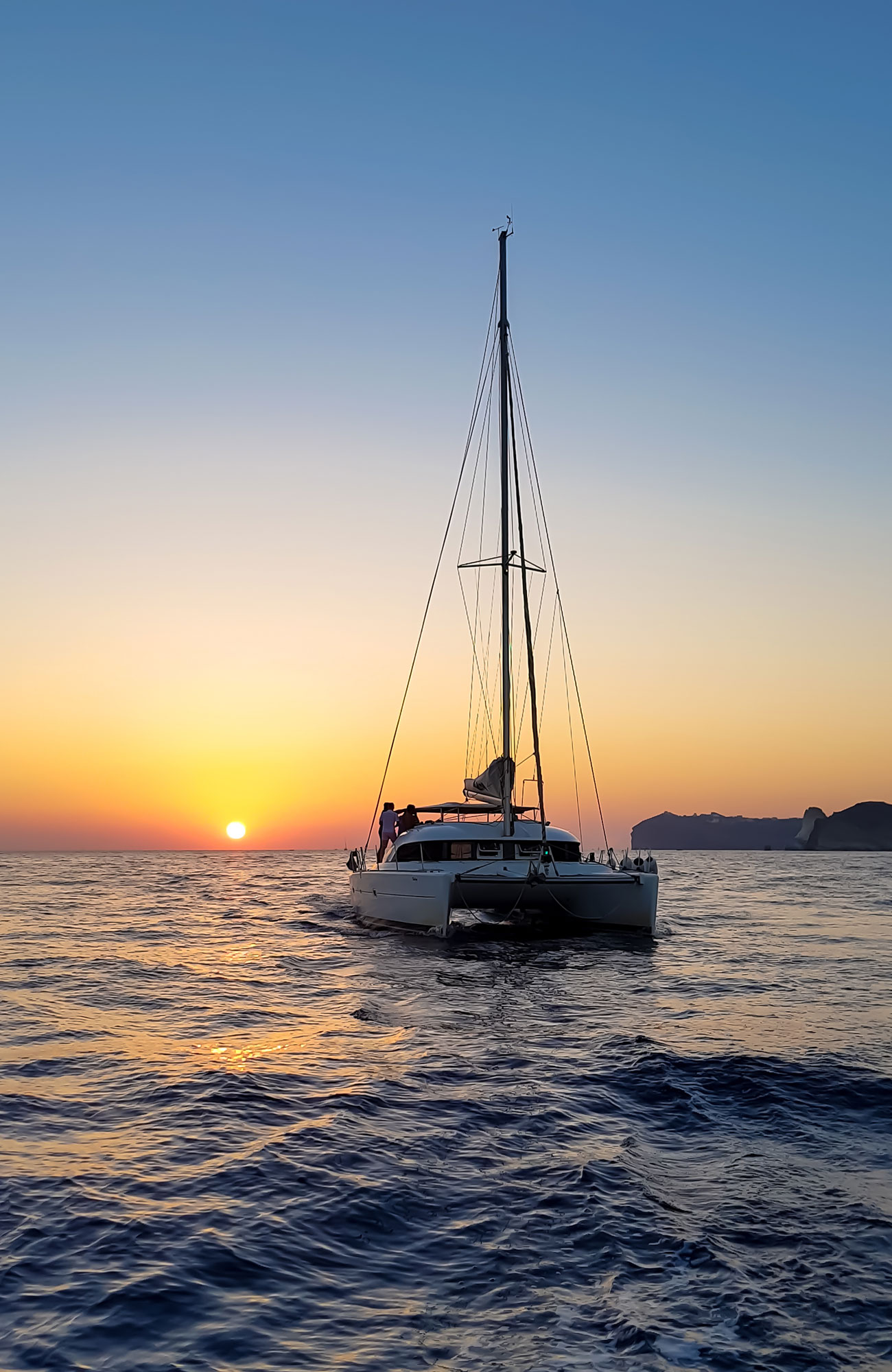 En man som båtluffar ligger i fören på en segelbåt i solnedgången. 