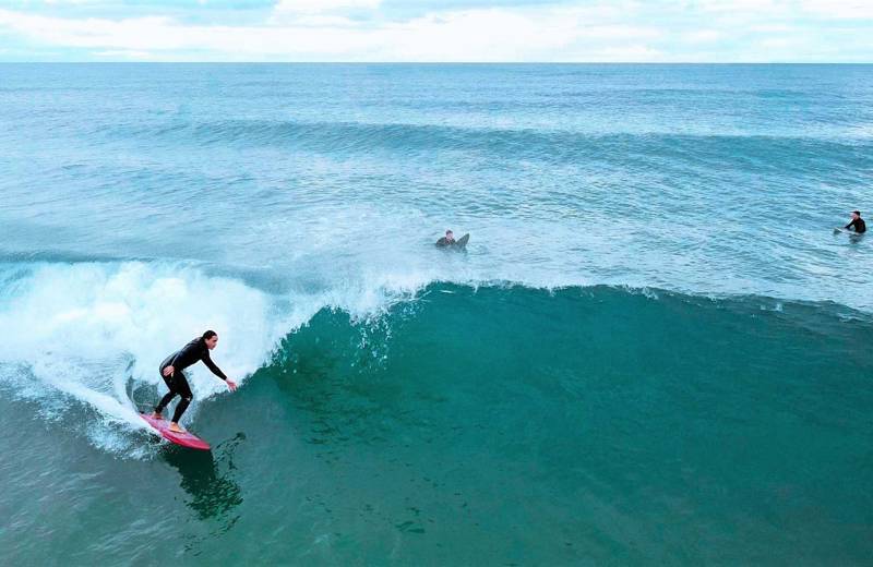Girl with black swim suit and pink surf board on wave
