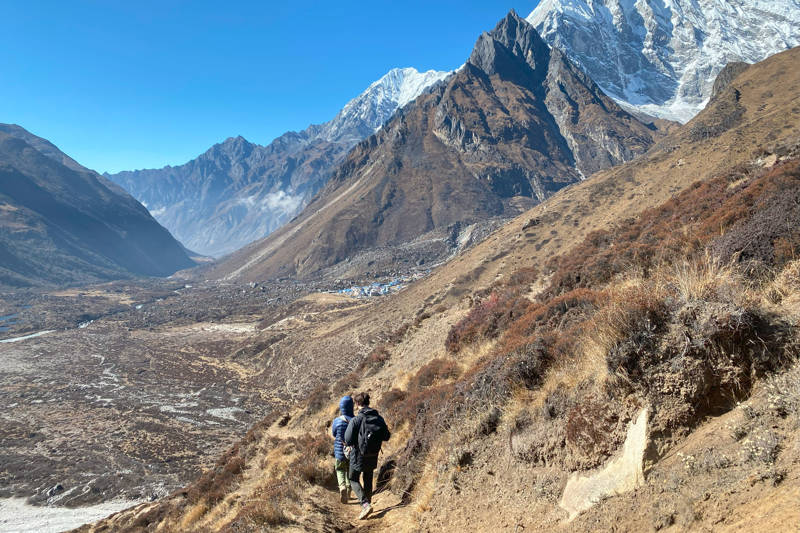 Group of guys hiking down a trail in the Himalayas in Nepal. In the background you can see the snow-covered Himalaya mountaintops