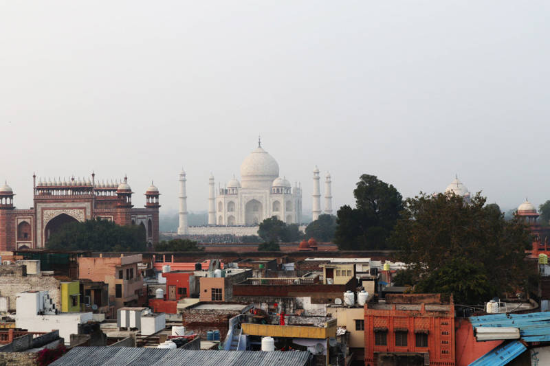 The big Taj Mahal with a foggy sky in the background, and colourful houses in the foreground of the picture.