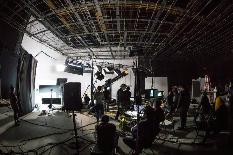 Behind the scenes of a film production with lots of people working on equipment, cameras and light set-ups
