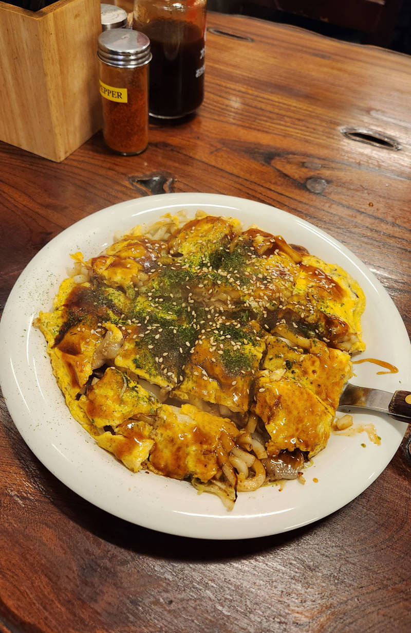 Platter of okonomiyaki, a savory pancake/omelett crossover with noodles, vegetables and sauce.