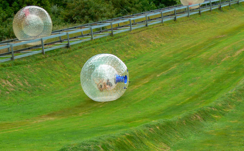 People trying out Zorbing in New Zealand on a green hill